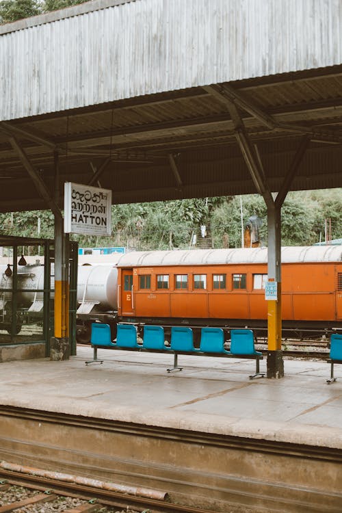 Modern railway platform with bench under roof and industrial train on railroad tracks on background on daytime