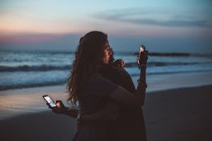 Couple hugging and using smartphone near sea on sunset