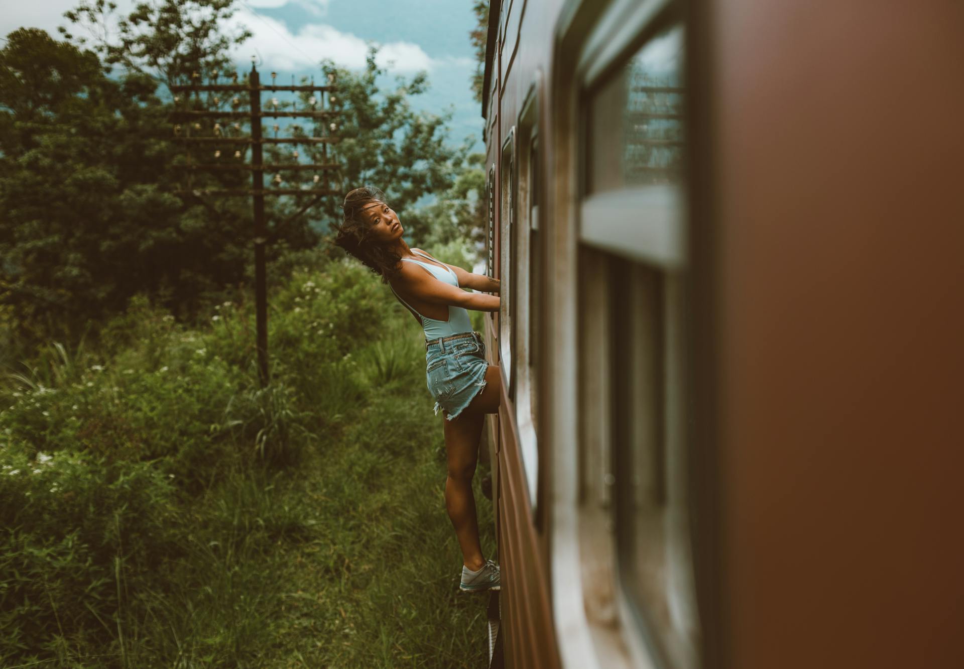Woman enjoying a thrilling train ride, leaning out a window amidst lush greenery.