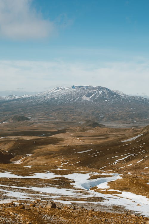 Free Land partly covered with snow located near mountain range under blue sky with clouds Stock Photo