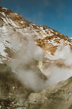 粗糙的山坡上布满石头和积雪，火山蒸汽在蓝天下喷向空中