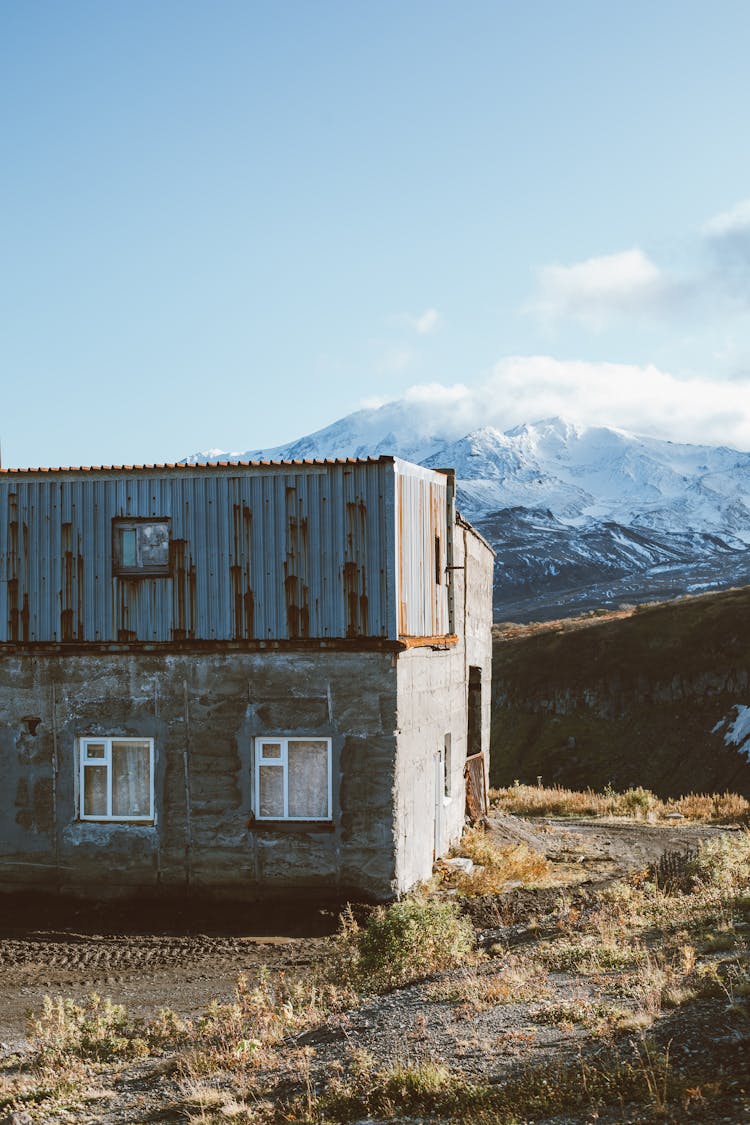 Stone House Against Snowy Mountain On Remote Highland