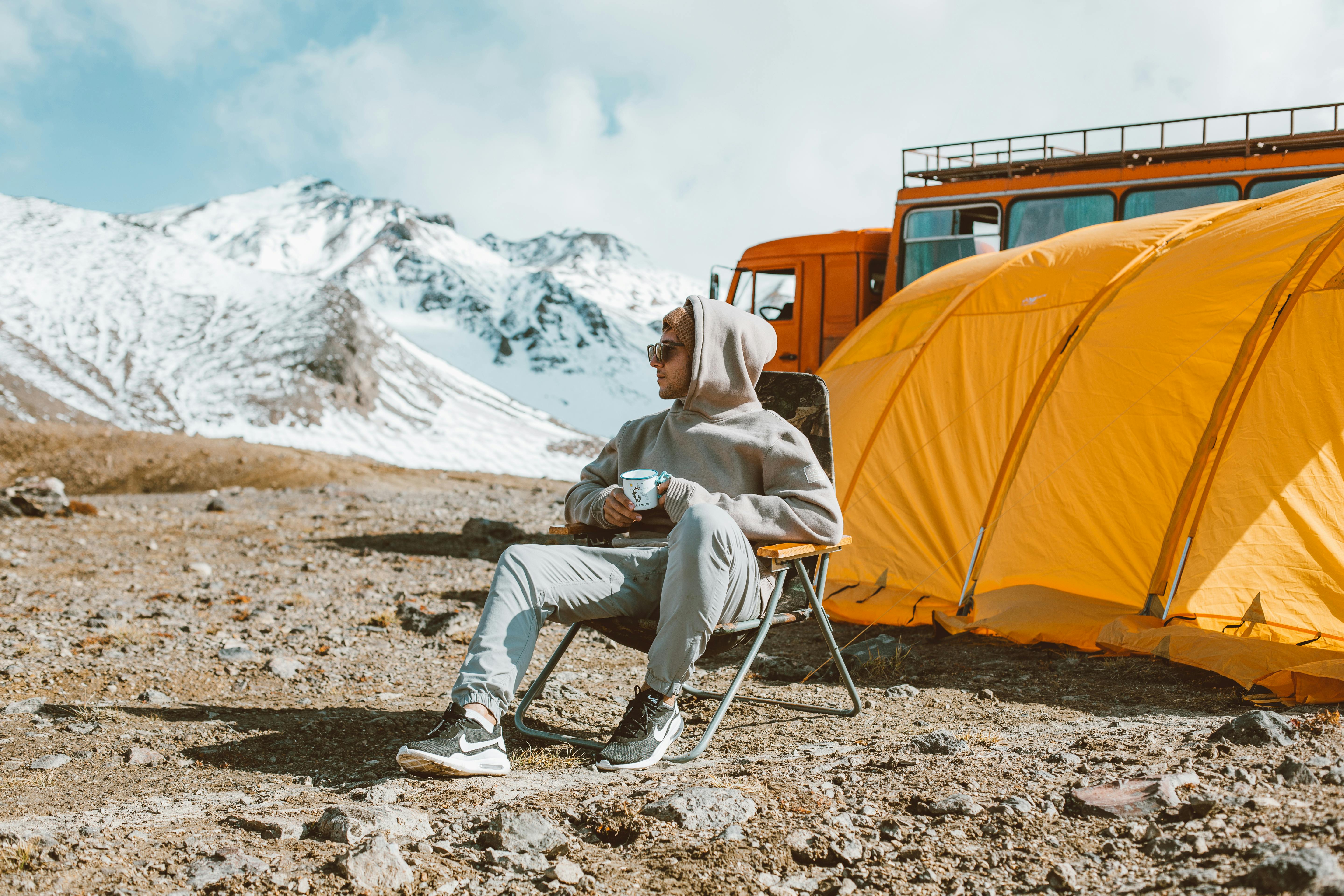 man sitting near camping and looking at mountain view