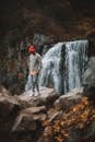 Full length of faceless man standing on stone on edge of cliff with and large waterfall on background