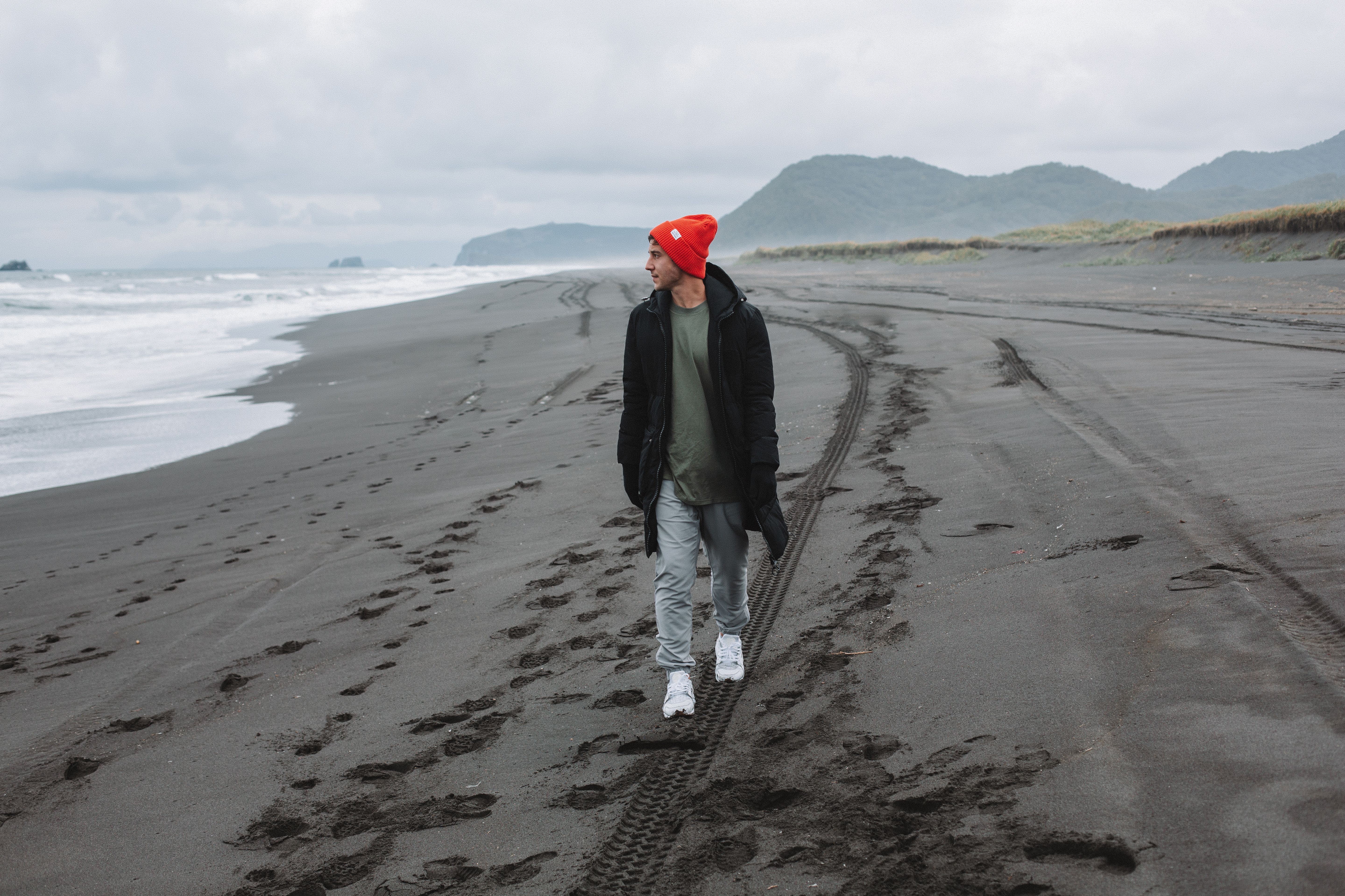 阴天，一个穿着温暖衣服的年轻人在荒无人烟的海滩上漫步，拥抱自由与自然