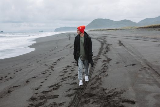 阴天，一个穿着温暖衣服的年轻人在荒无人烟的海滩上漫步，拥抱自由与自然