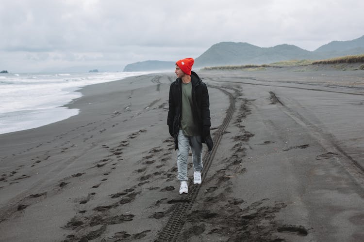 Male Tourist Walking Along Empty Beach And Admiring View On Ocean