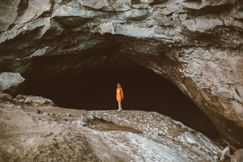 Full body of faceless person in warm clothes standing alone in dark cave of large stone mountain