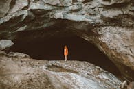 Full body of faceless person in warm clothes standing alone in dark cave of large stone mountain