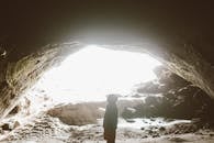 Side view of unrecognizable traveler standing in mountain cave in light of bright sun and admiring stone formation