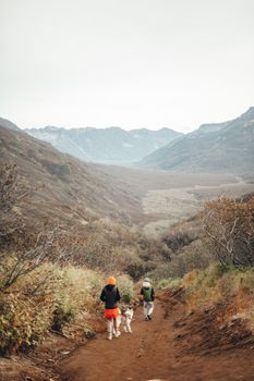 徒步旅行者带着他们的狗，沿着一条风景如画、被山脉和秋叶环绕的山谷小路探索前行