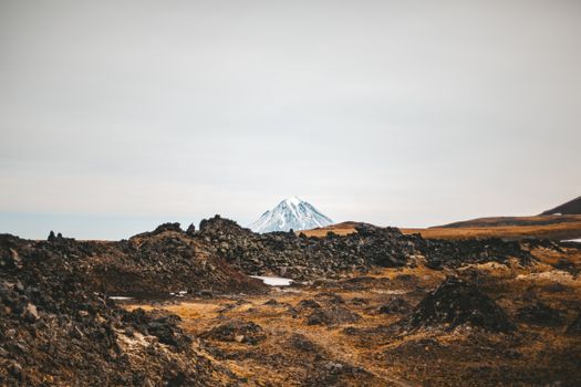 白雪皑皑的山峰矗立在多云天空下，周围环绕着崎岖的火山地形