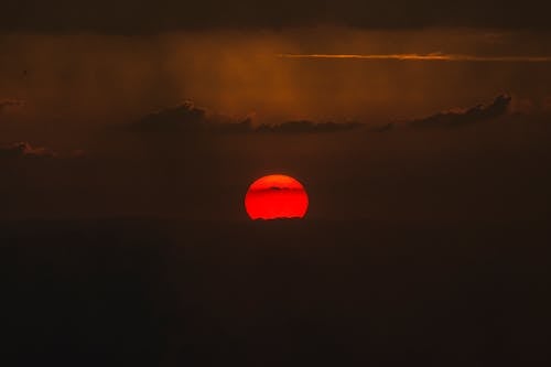 Red sun rising over horizon in cloudy sky above mountain range during sundown time in darkness in foggy weather outside