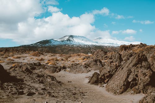 Picturesque view of distant mountains with snow on slopes surrounded by rocky terrain under cloud sky