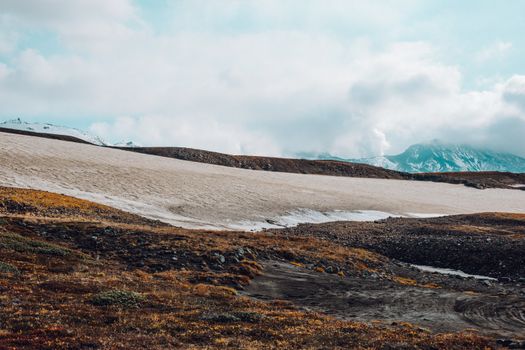 Picturesque Nordic landscape of snowy mountains and hilly valley with sparse vegetation under sky with clouds during daytime