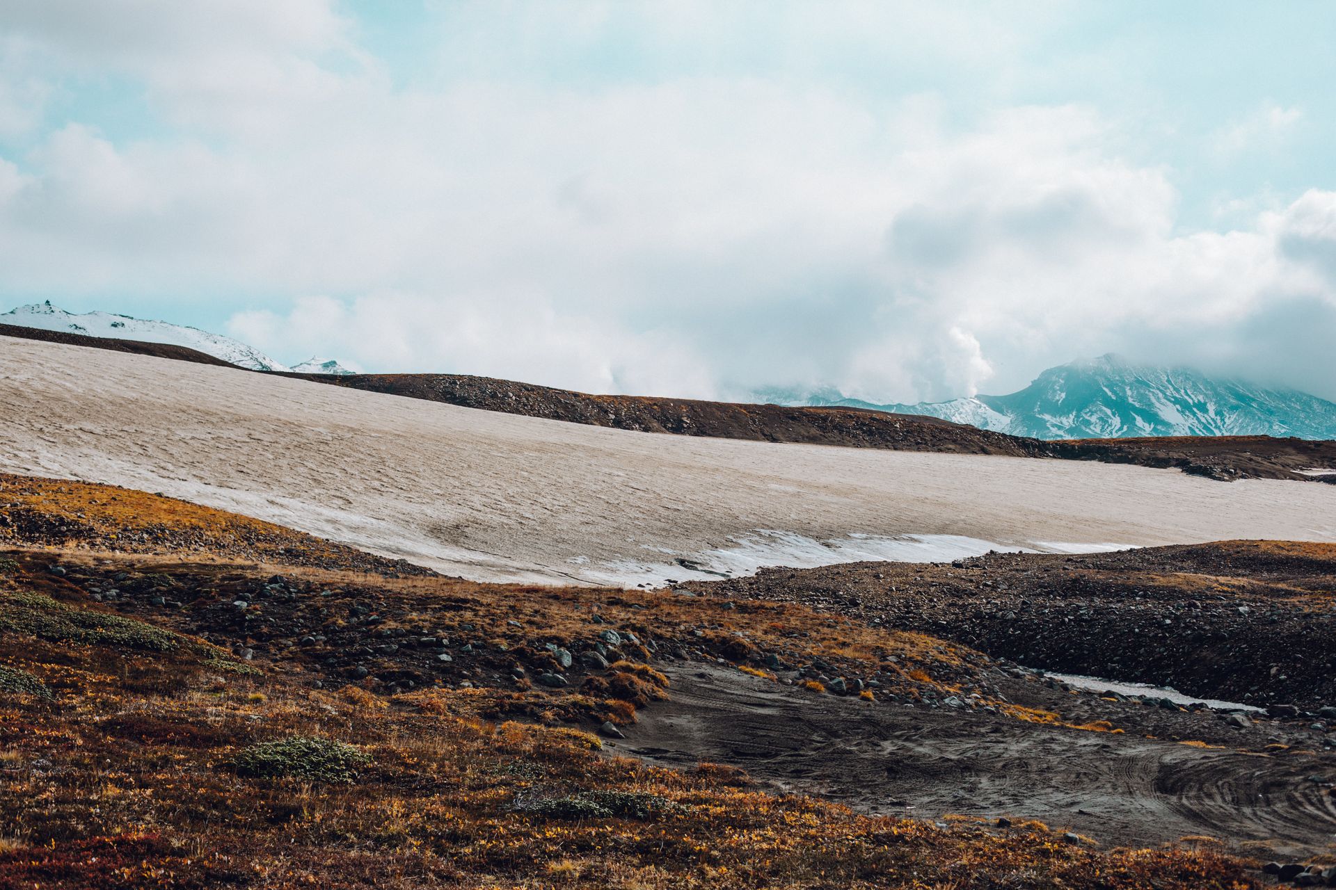 Picturesque Nordic landscape of snowy mountains and hilly valley with sparse vegetation under sky with clouds during daytime