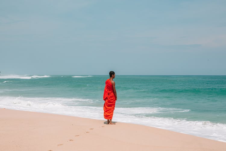 Unrecognizable Asian Man In Traditional Orange Cloth On Beach