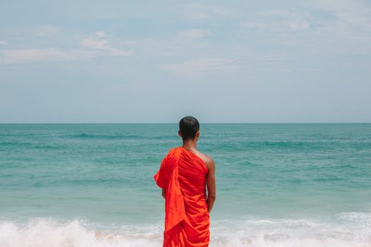 一位僧人穿着鲜艳的橙色长袍，平静地站在海边，象征着宁静和沉思