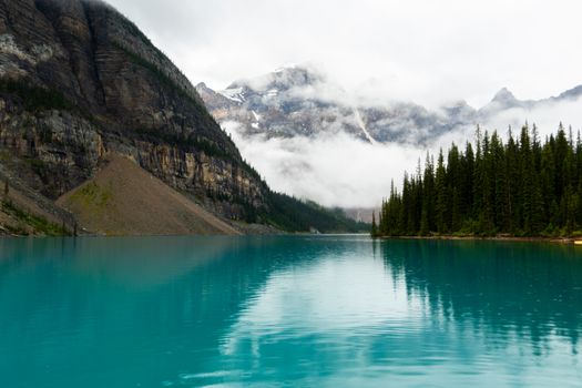 Beautiful view of Moraine Lake in Banff, Canada, with foggy mountains and crystal blue waters creating a serene atmosphere.