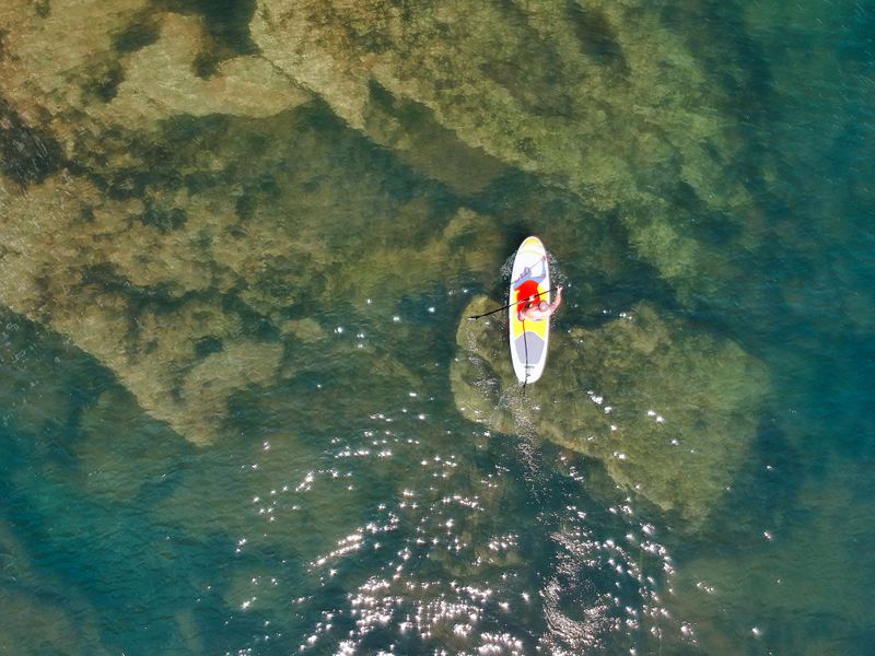 Vista aérea de paddle surf sobre aguas cristalinas con el fondo marino visible