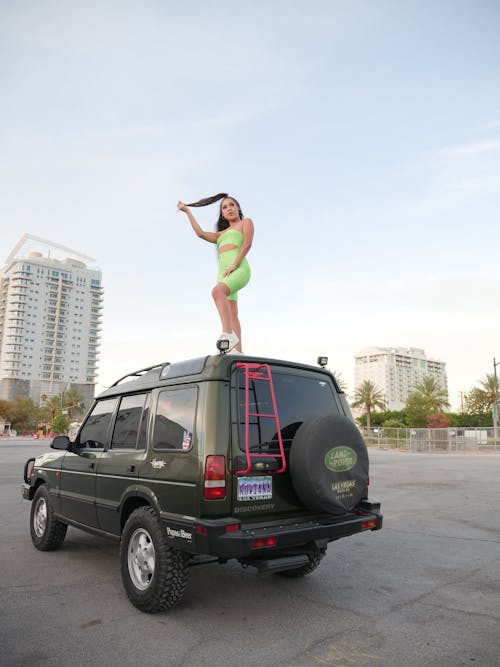Woman in Green Gym Wear Standing on Vehicle Roof