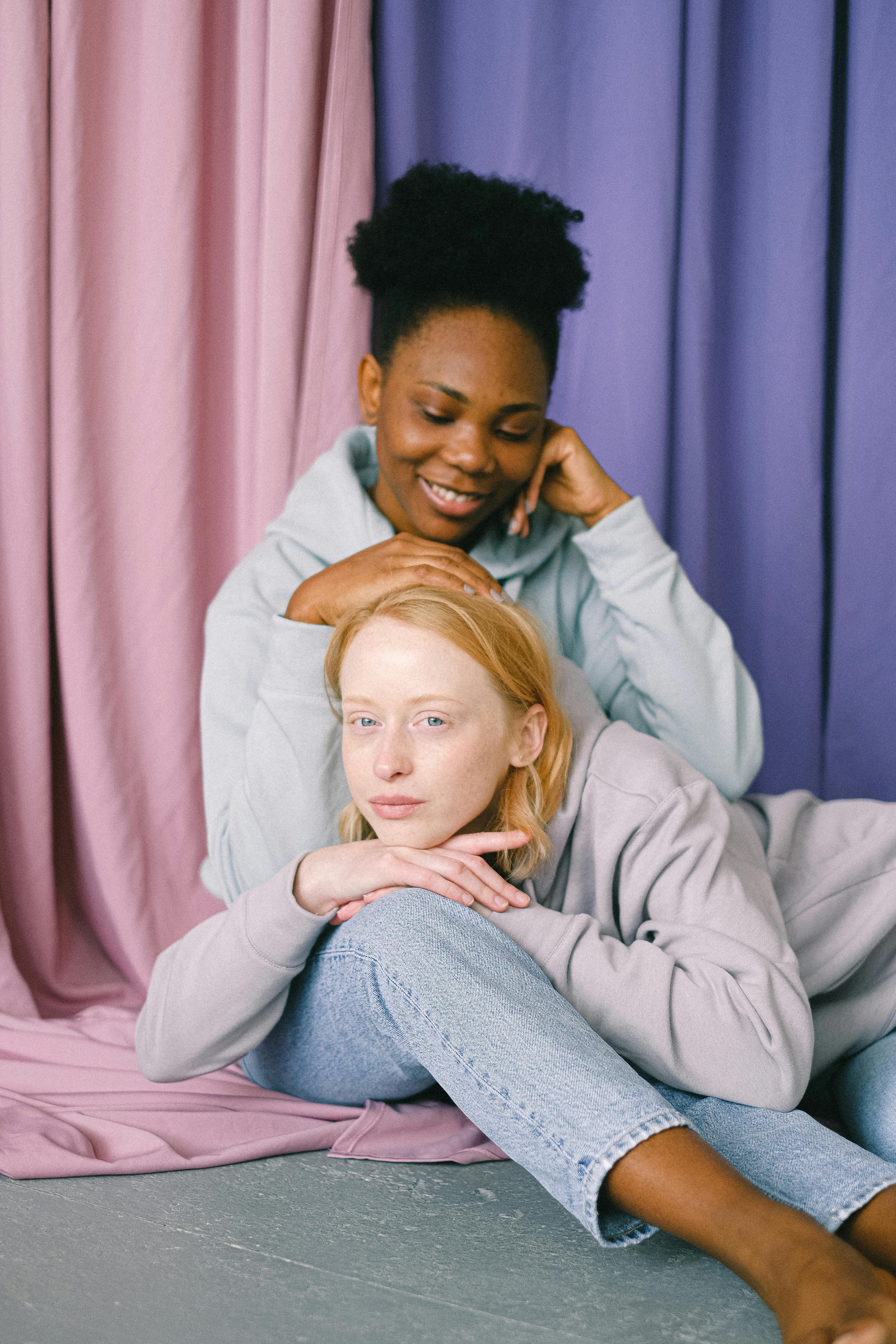 A smiling, interracial couple sitting together in front of pastel curtains, showcasing affection and diversity.