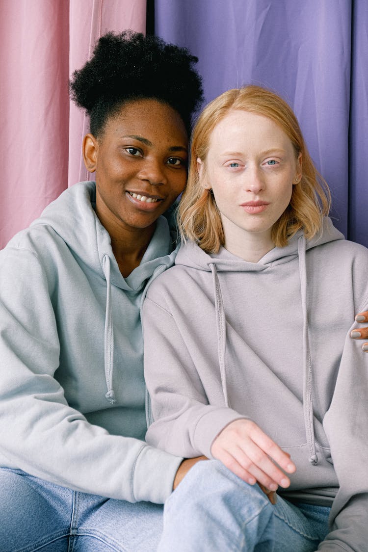 Women Wearing Hoodies Sitting Beside Curtains