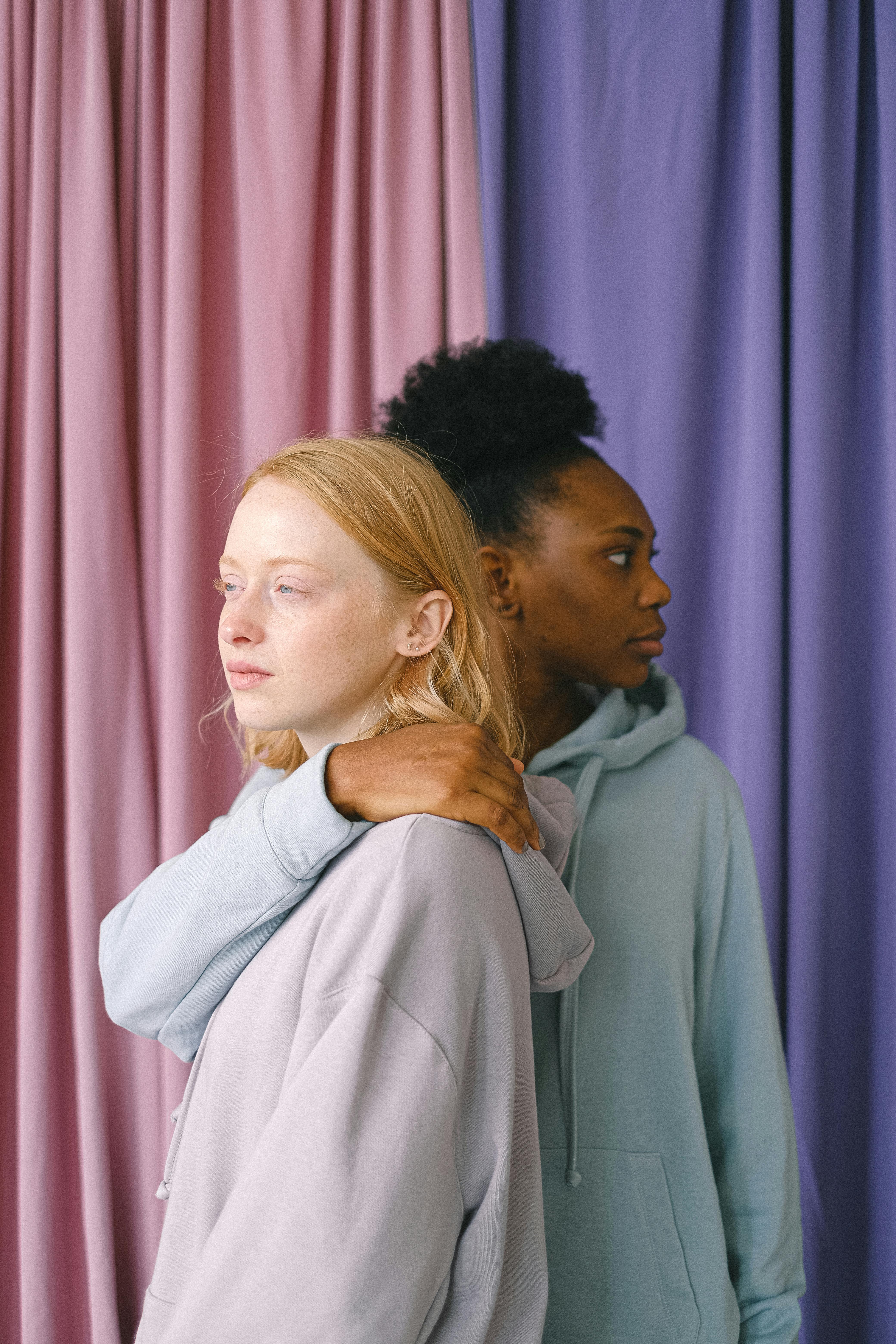 在色彩缤纷的窗帘下，两名女性相拥，展现了友谊与多样性