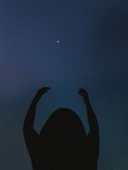 漆黑的夜空中，一个人举起双手，剪影对着月亮