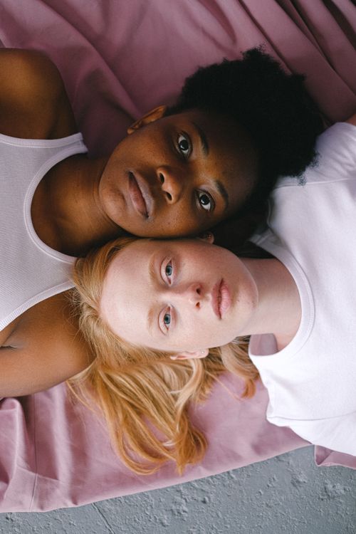 Free Two women, one black and one caucasian, lying on pink fabric wearing white tank tops. Stock Photo