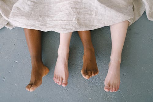 Free Bare Feet Coming out of Bed Sheets Stock Photo