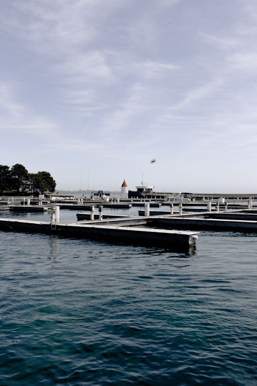 Free Serene view of an empty marina with blue waters under a clear sky, featuring docks and a distant lighthouse. Stock Photo