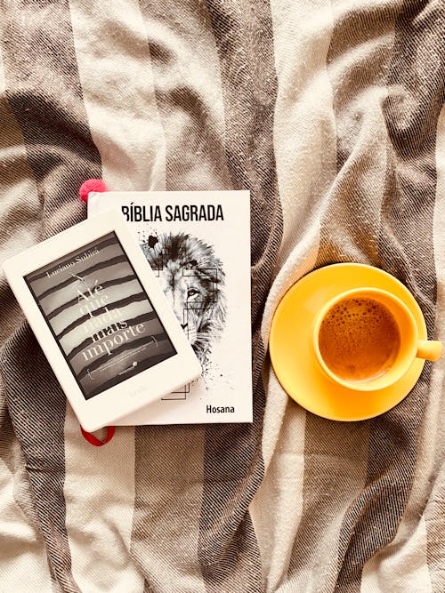 Cup of coffee arranged on bed with books