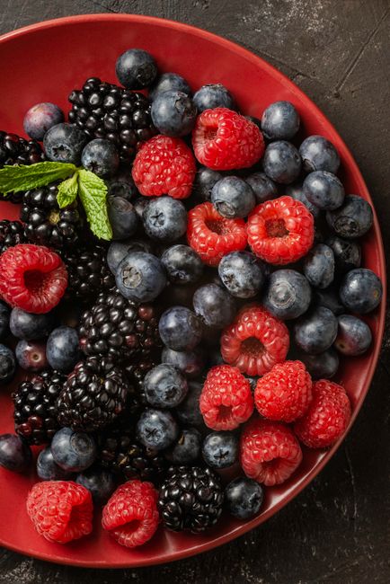 From above of delicious appetizing mixed red and black berries placed in red ceramic plate on brown surface as healthy organic dessert