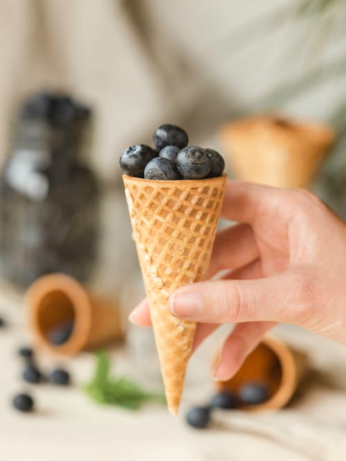 Anonymous woman taking waffle cone with blueberries