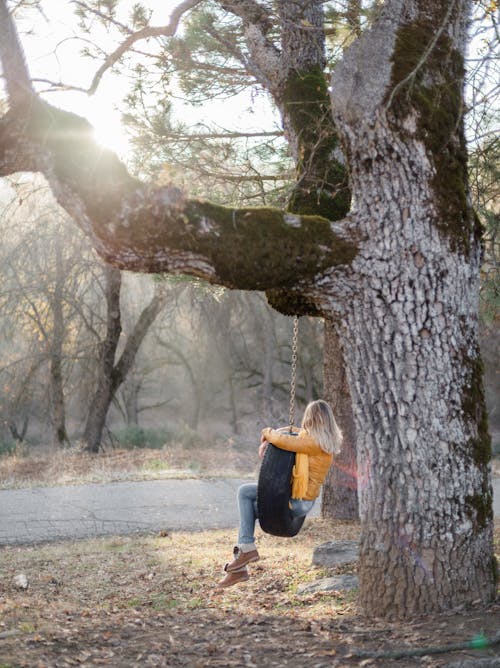 Free Anonymous lady in warm clothes on tire swing in autumn Stock Photo