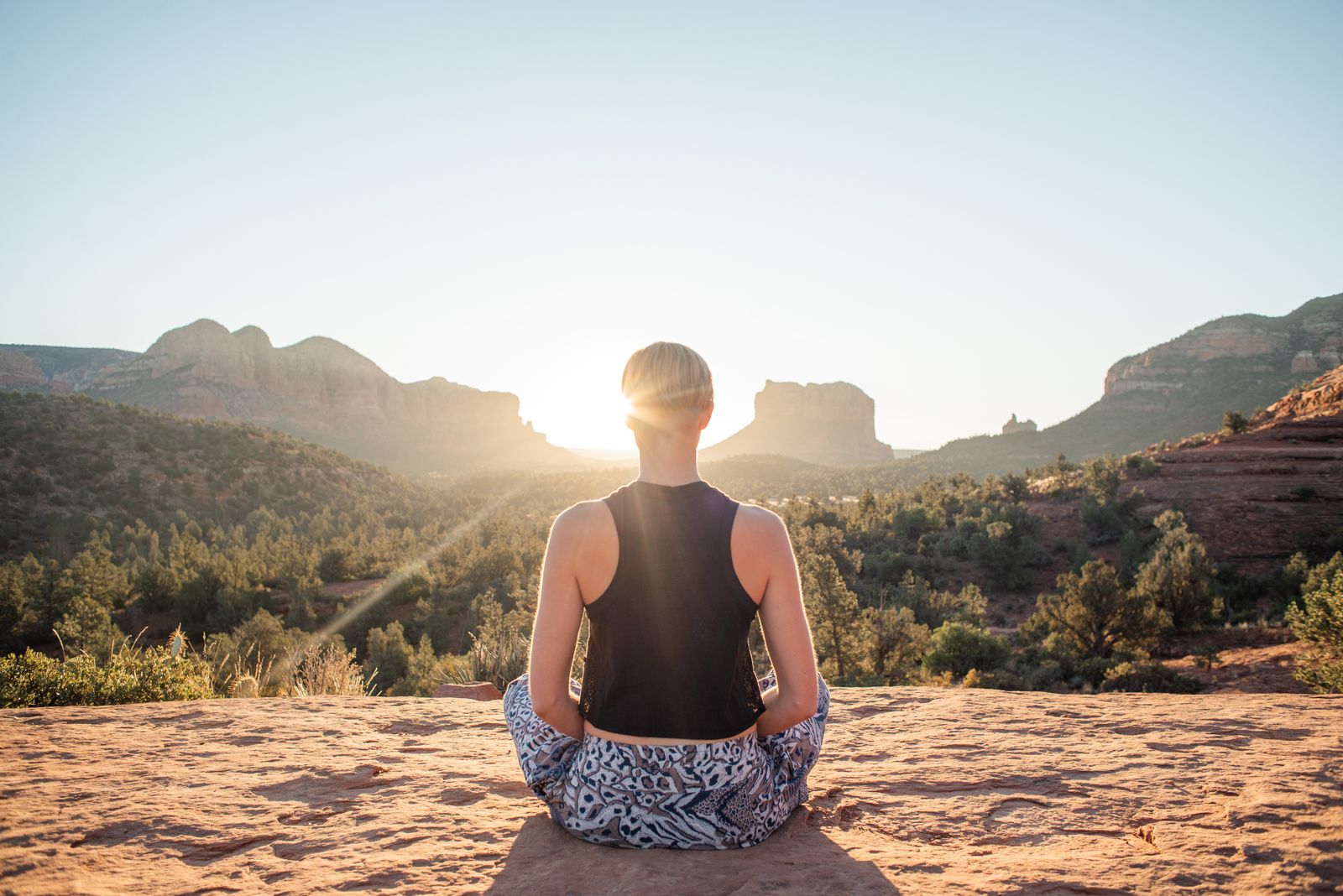Woman sitting in lotus pose meditating on a sunlit cliff at sunrise, illustrating the meditative focus of kriya yoga practice