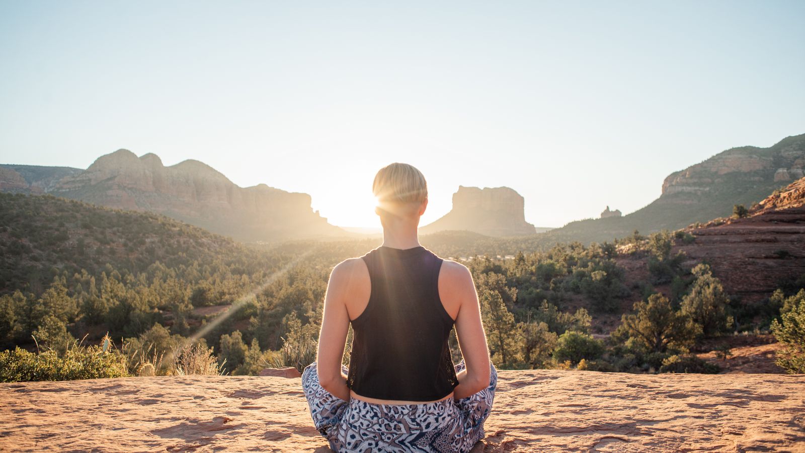 A woman meditating in lotus pose on a sunlit cliff at sunrise