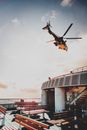 Low angle of contemporary helicopter flying above industrial ship floating in sea at sunset