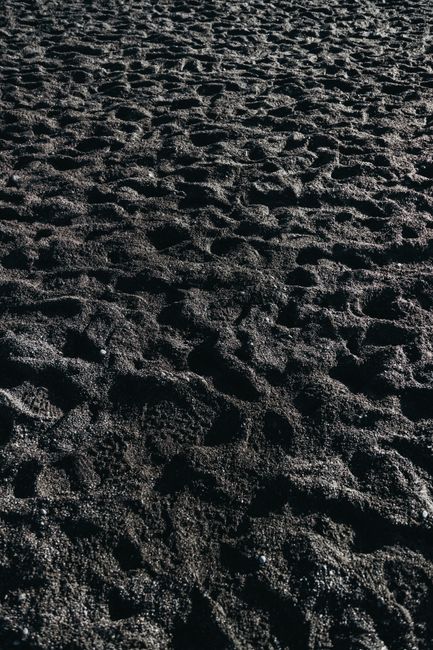 From above of dark uneven surface of rocky coast covered with tiny pebbles in daylight