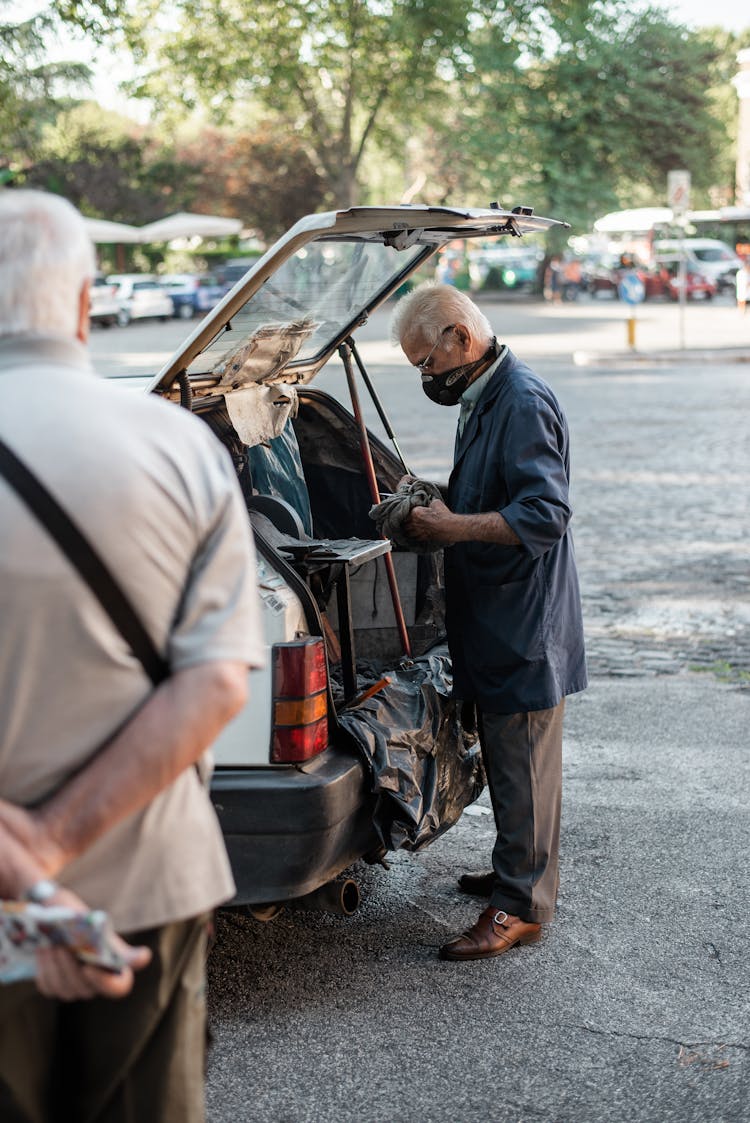 Male In Face Mask Taking Things Out Of Car Trunk