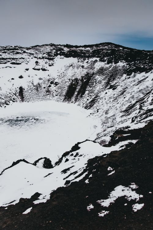 Free From above of picturesque crater covered with snow located in volcanic mountains against cloudy sky Stock Photo