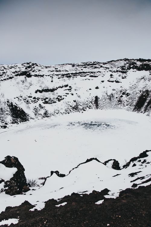 Free From above of pit covered with snow  and hoarfrost located amidst rocky mountains against gray sky during winter day in nature Stock Photo