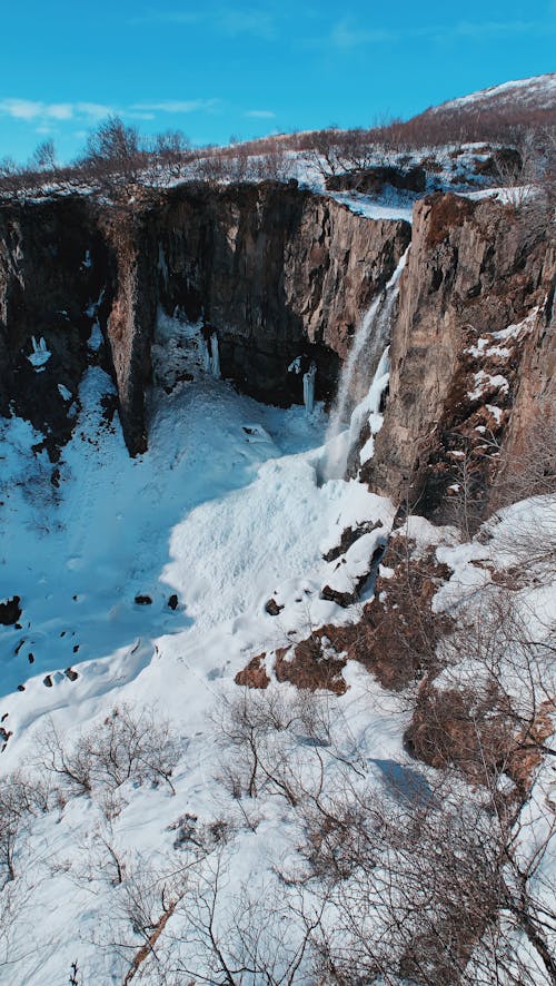 Majestic view of cliff with leafless bushes located on snowy area against blue sky in sunny day in winter time