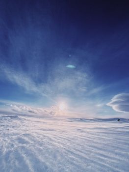 Picturesque view of empty field covered with snow against cloudy sky with bright sun during winter day in cold weather