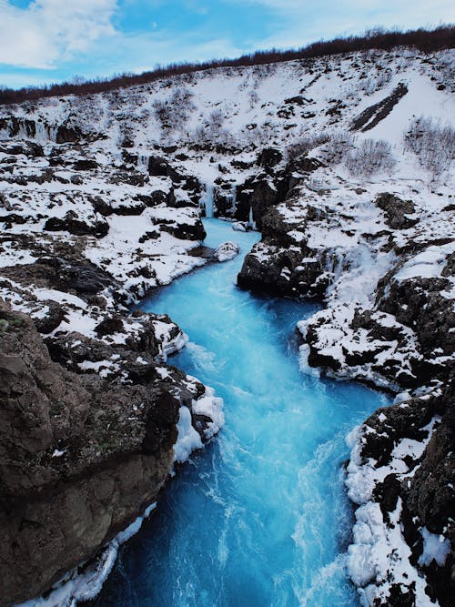 From above of steep coast covered with snow located among lake against blue sky during winter day in cold weather