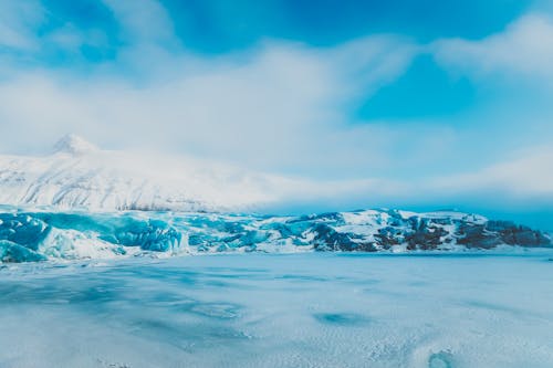 Severe scenery of frozen water with hoarfrost located near mountain ridge covered with snow against cloudy sky in cold day