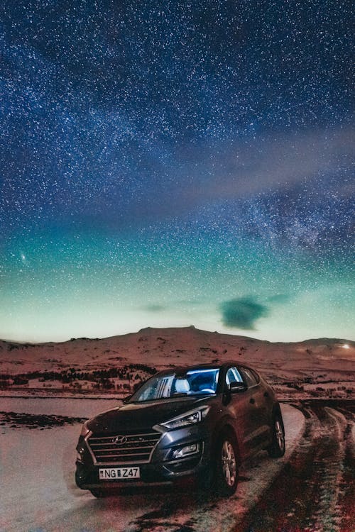 Modern vehicle parked on roadside near mountain terrain under colorful starry sky in sunset time in nature in summer evening