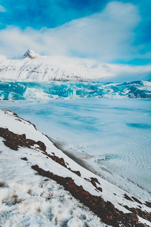 Free Majestic view of frozen sea located near snowy peaks against cloudy sky during winter time in daylight in sunny nature Stock Photo