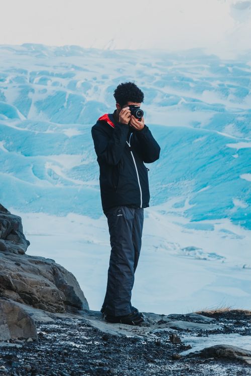 Free Faceless male camper standing on stony ground near snowy surface and taking photos of scenery in winter time in daytime Stock Photo
